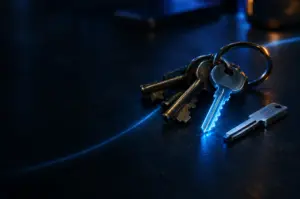 A ring of brass keys on a dark desk, one freshly cut duplicate key glowing faintly blue